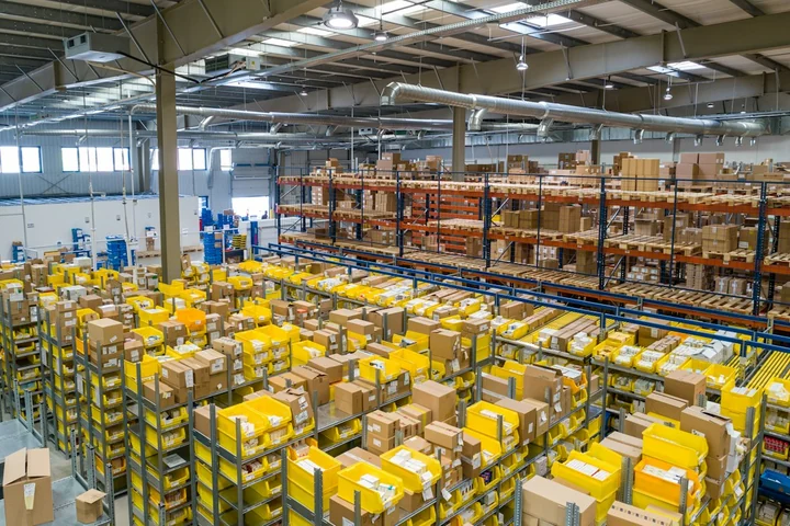 Warehouse shelves filled with parcels and boxes beneath overhead lighting