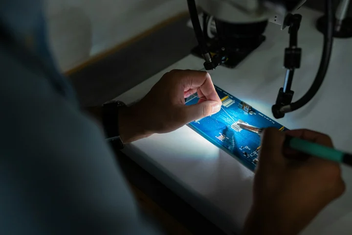 Technician inspecting an electronic circuit board beneath a microscope